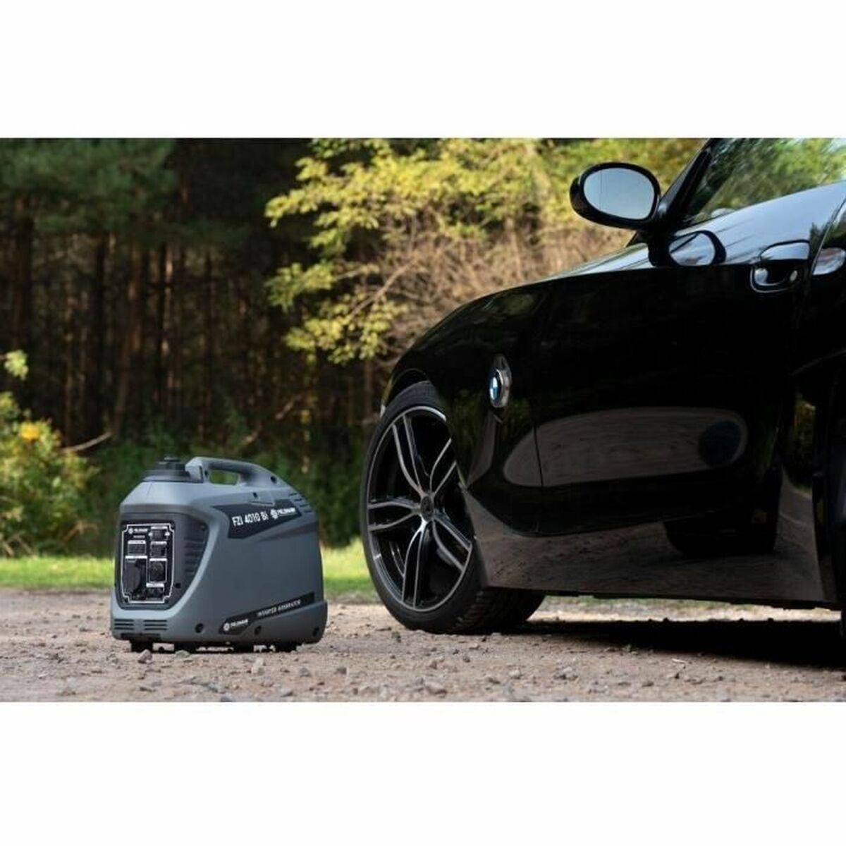 Fieldmann FZI 4010-Bi inverter aggregaat naast een zwarte auto op een grindpad in een bosrijke omgeving